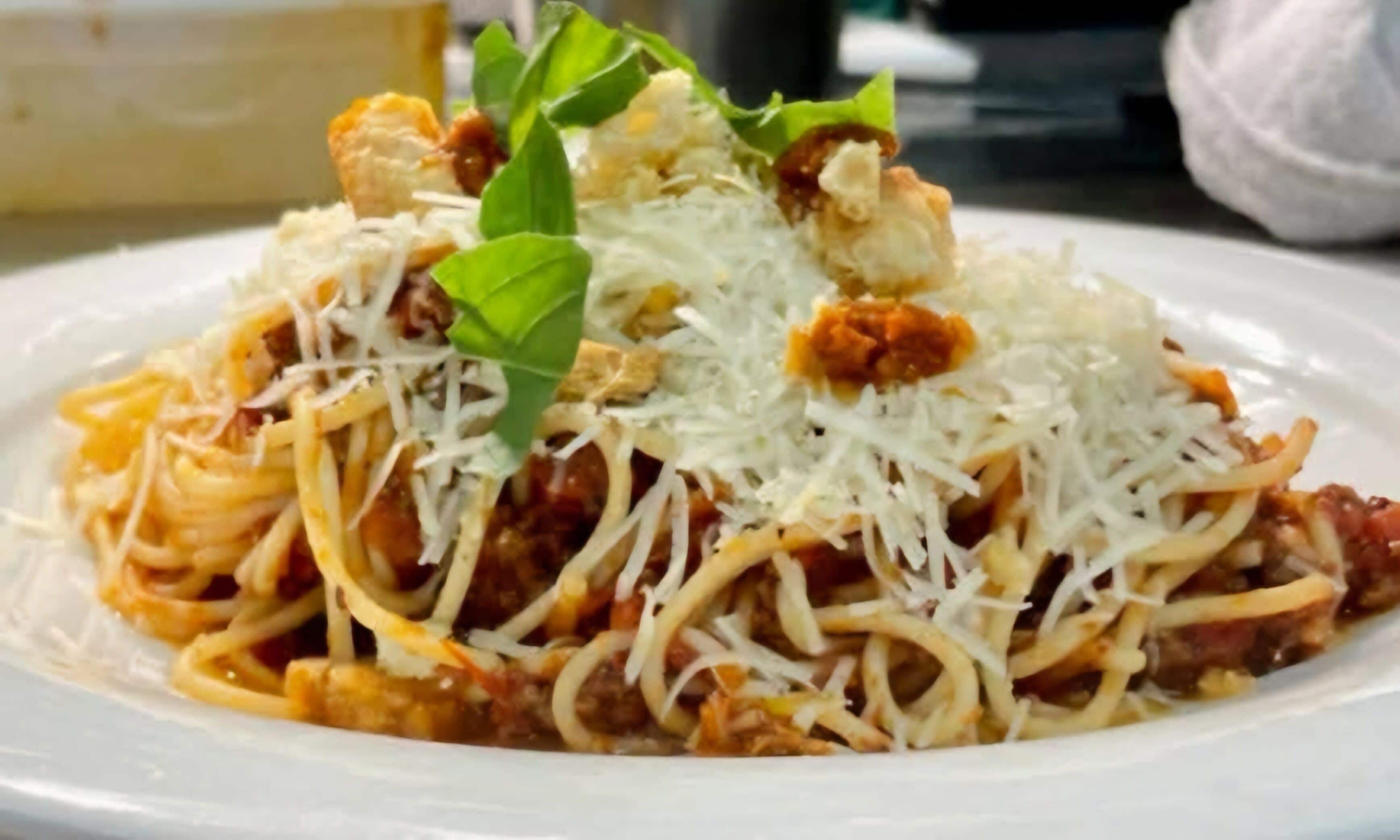 A plate of spaghetti with tomato sauce, cheese, and basil.