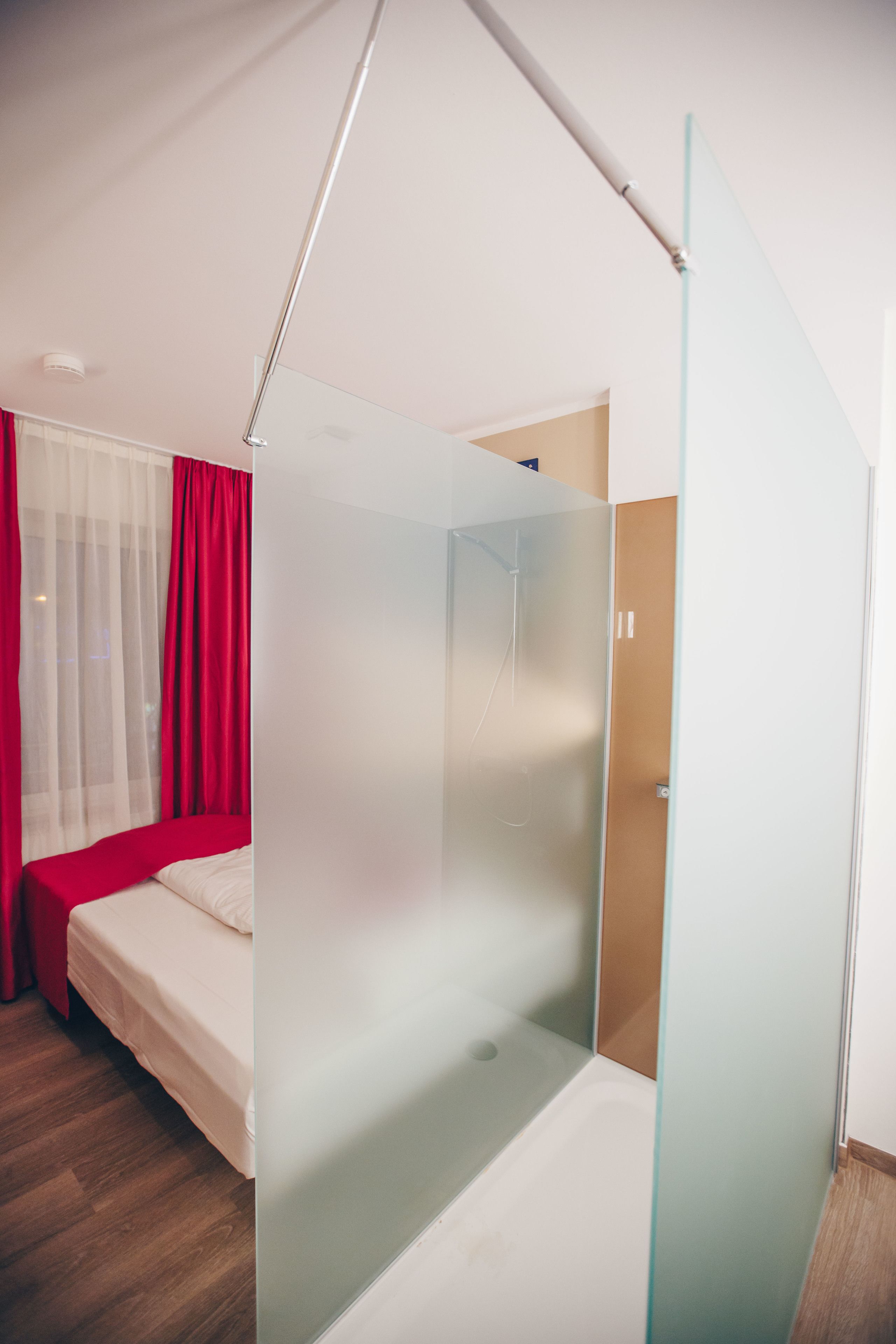 A modern bedroom with a glass partition, a bed with white bedding, and a wooden floor.