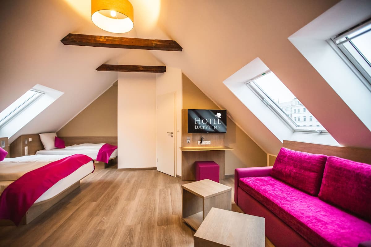 A modern hotel room with two beds, a sofa, a TV, and skylights.