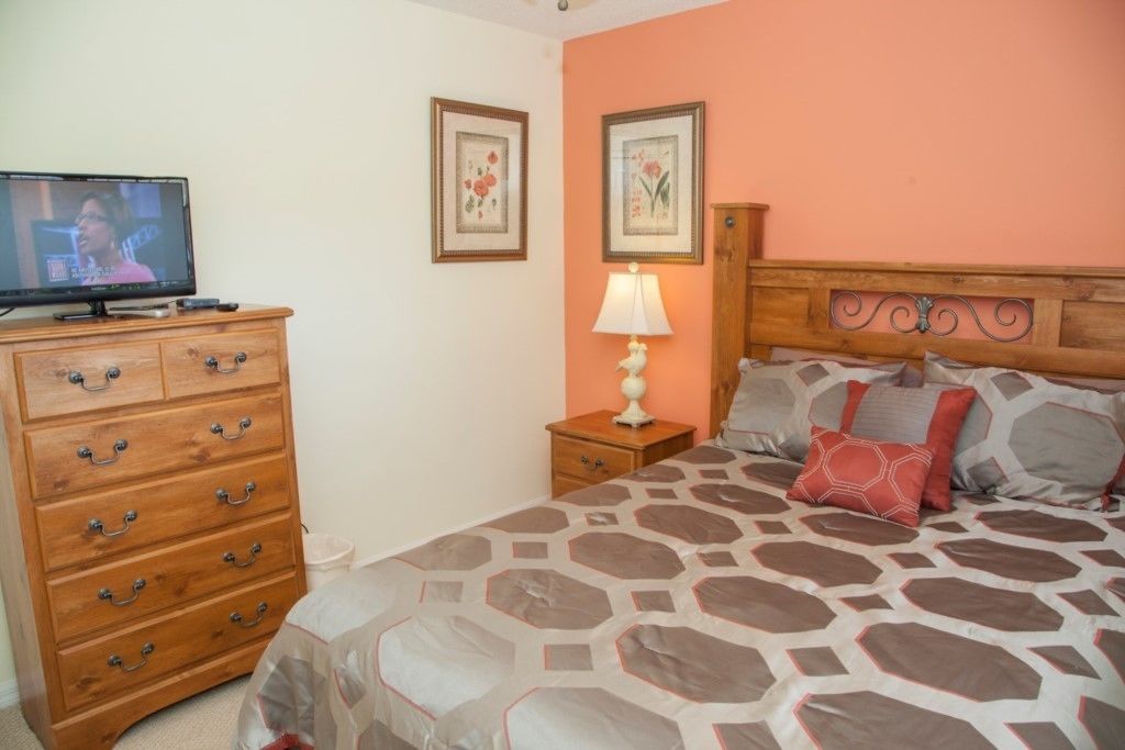 A bedroom with a bed, wooden dresser, nightstand, and a television on the dresser.