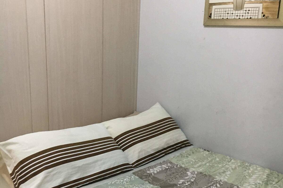 Un lit simple avec des oreillers à rayures et une couvre-lit à motifs floraux, dans une pièce dont le mur est uni et qui est décorée d’un tableau encadré.