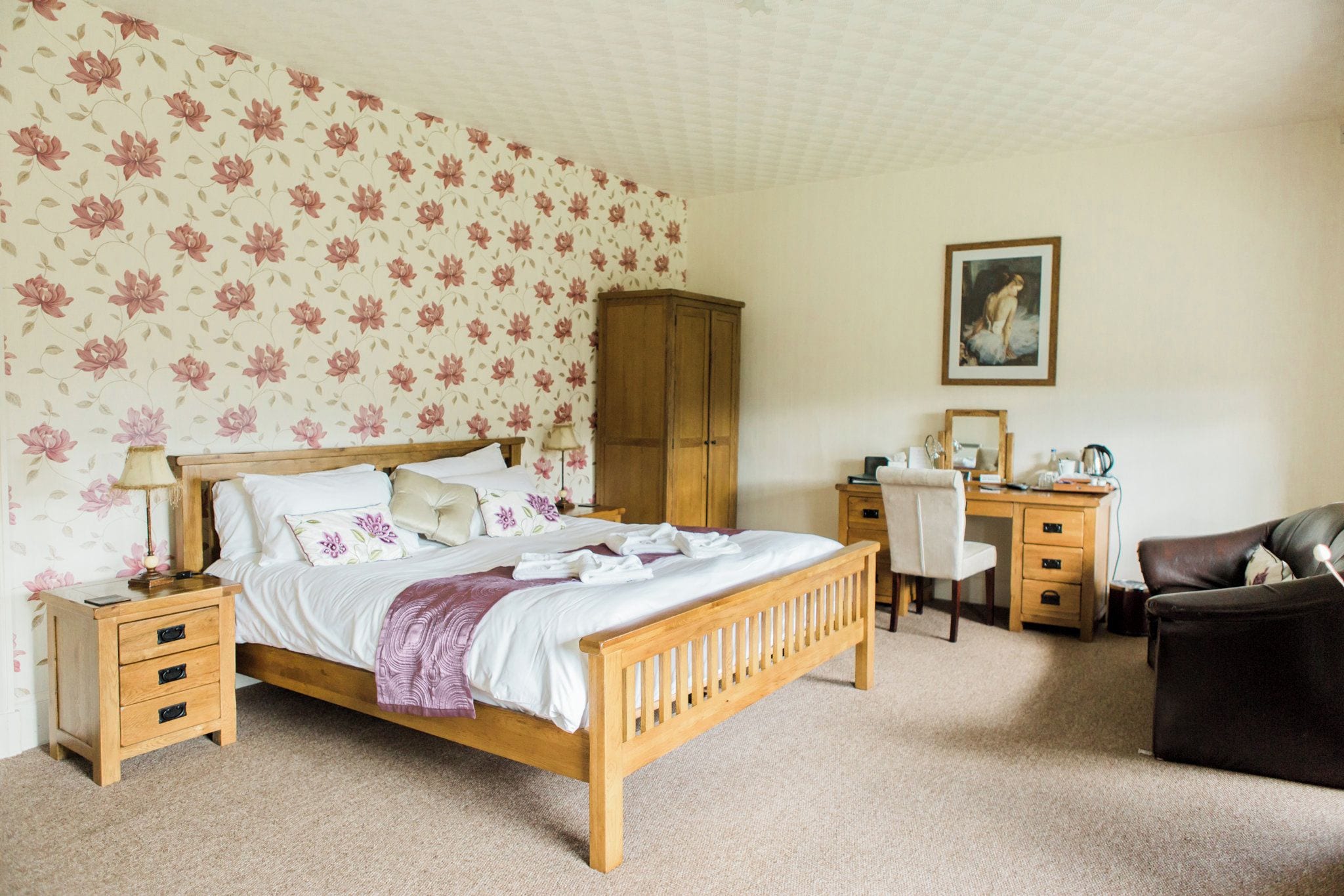 A bedroom with a wooden bed, a desk, a chair, a wardrobe, and a painting on the wall.