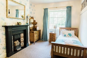 A bedroom with a wooden bed, a dresser, a mirror, a fireplace, and a window with curtains. - The Oakeley Arms Hotel (Blaenau Ffestiniog)