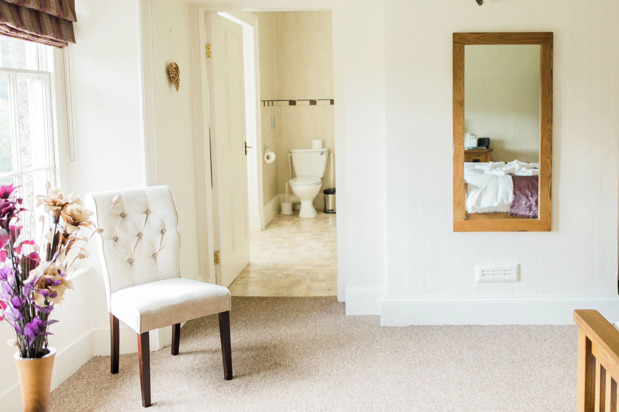 Ein Zimmer mit Stuhl, Spiegel und Blick ins Bad.