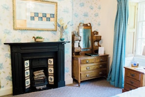 A room with a fireplace, a dresser with drawers, a mirror, and a window with curtains. - The Oakeley Arms Hotel (Blaenau Ffestiniog)
