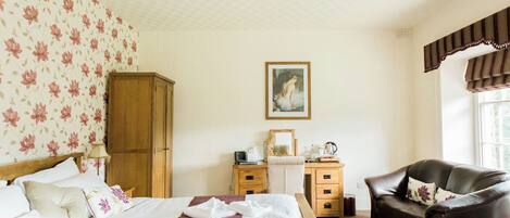 Un dormitorio con cama, armario de madera, escritorio con silla, un cuadro en la pared y ventana con cortinas.