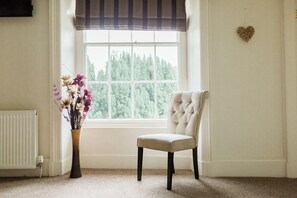 A room with a window, a radiator, a chair, and a vase with flowers. - The Oakeley Arms Hotel (Blaenau Ffestiniog)