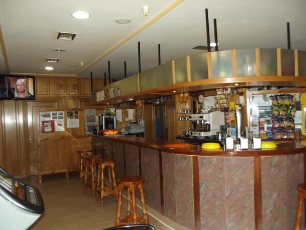 A bar area with wooden cabinets, a counter with stools, and a television screen. - La Montaña Palentina (Guardo)