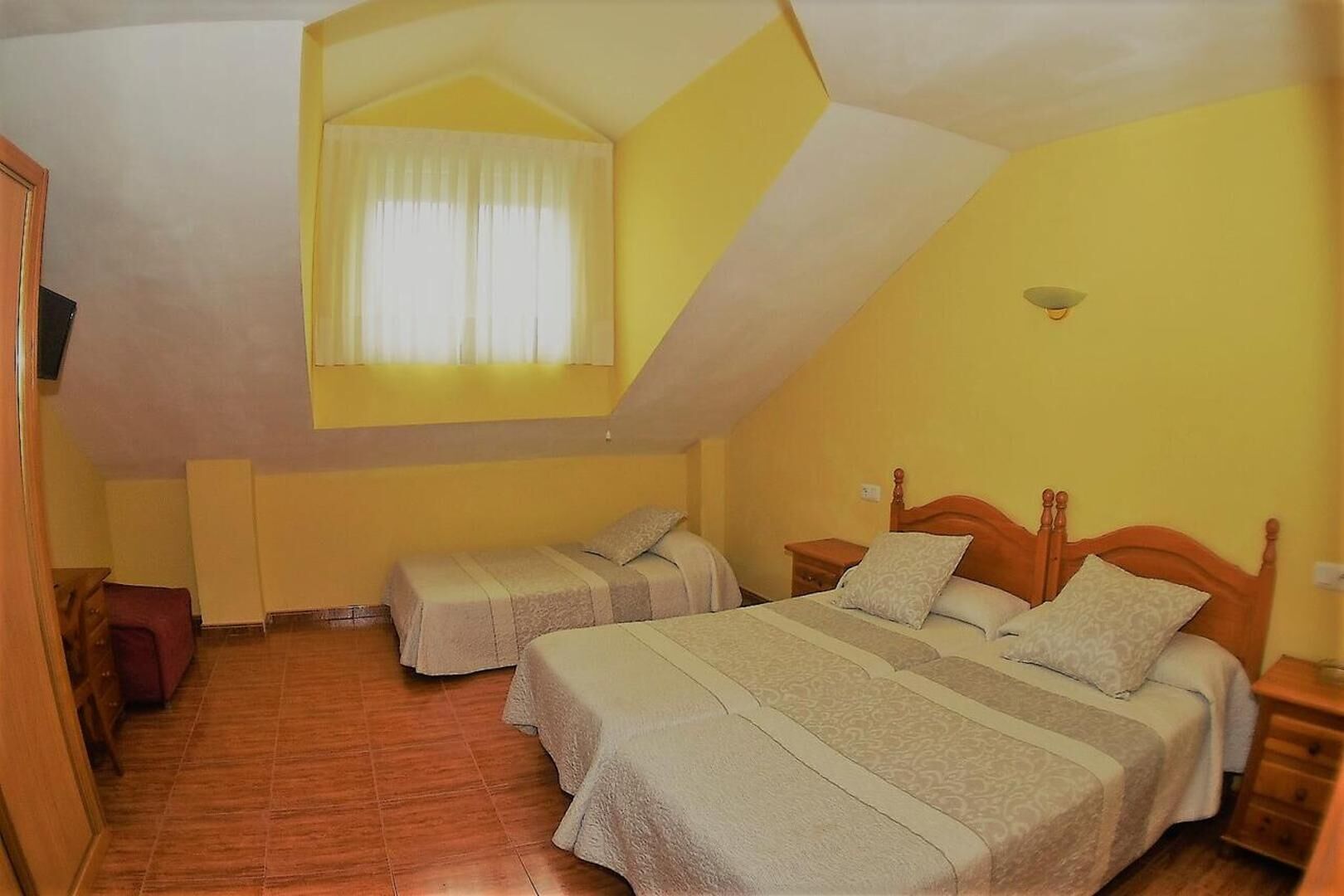 Una habitación con dos camas, techo inclinado y ventana con cortinas.