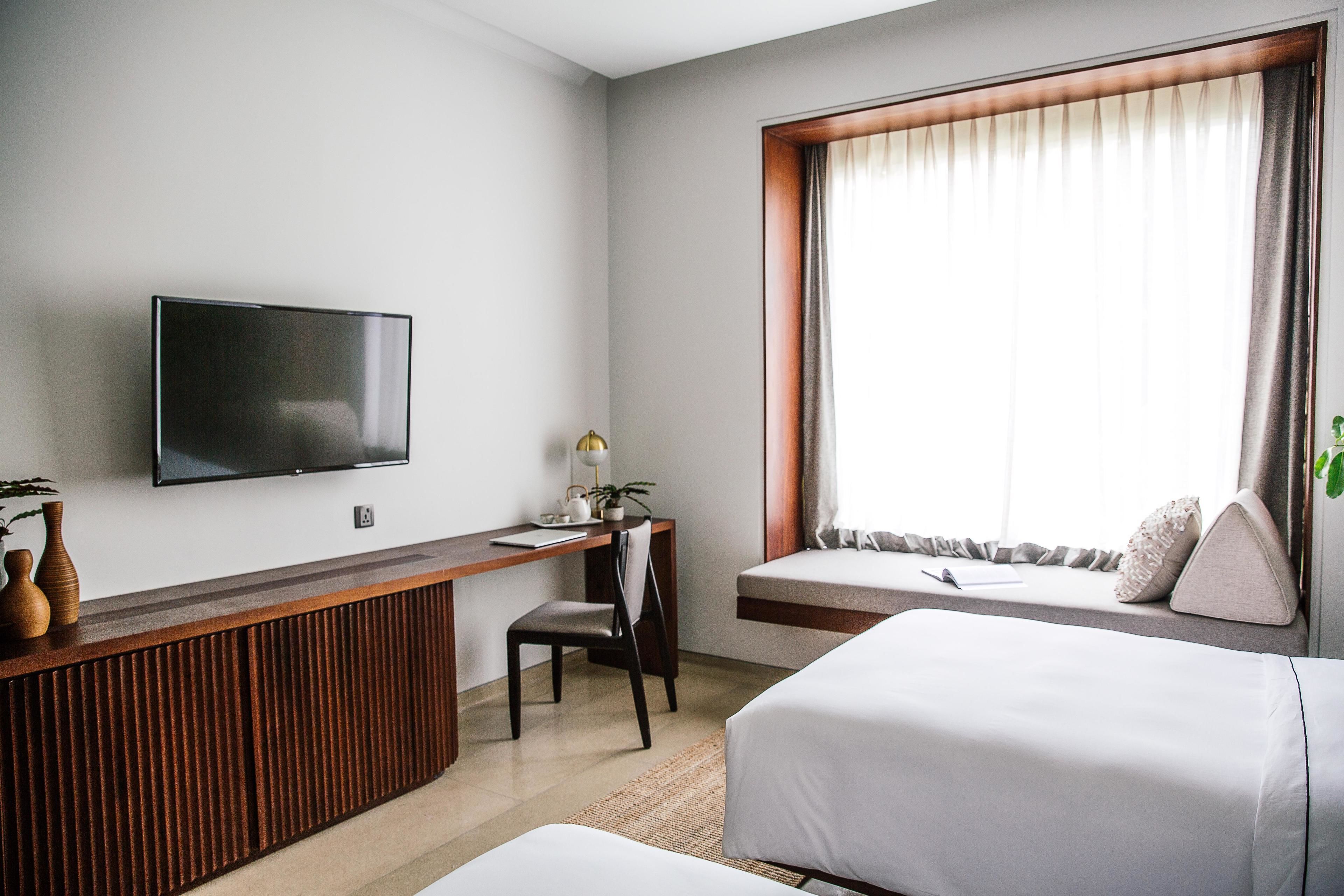 Ein Hotelzimmer mit Bett, Schreibtisch, Stuhl, Fernseher und einem Fenster mit Vorhängen.