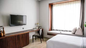 Ein Hotelzimmer mit Bett, Schreibtisch, Stuhl, Fernseher und einem Fenster mit Vorhängen.