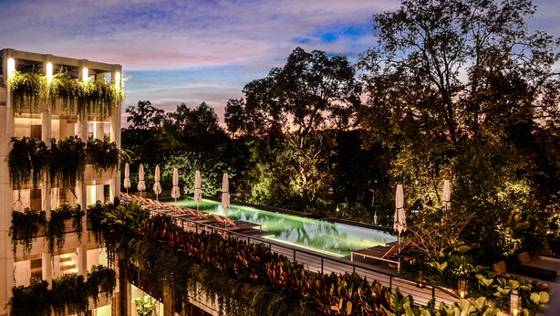 A rooftop pool with lounge chairs and umbrellas, surrounded by lush greenery and trees. - Treeline Urban Resort (Siem Reap)