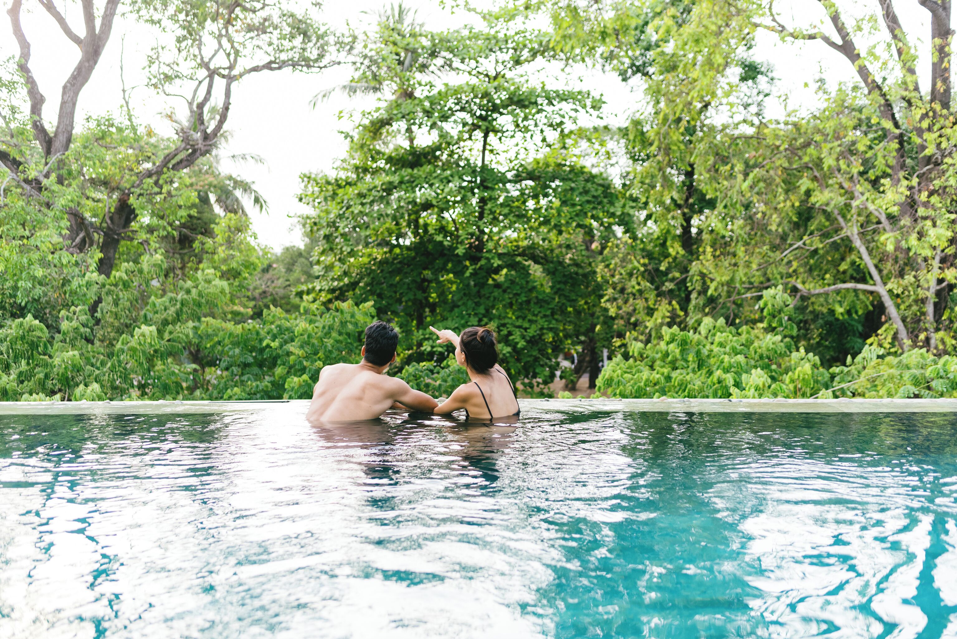 A couple in a swimming pool with lush greenery in the background.