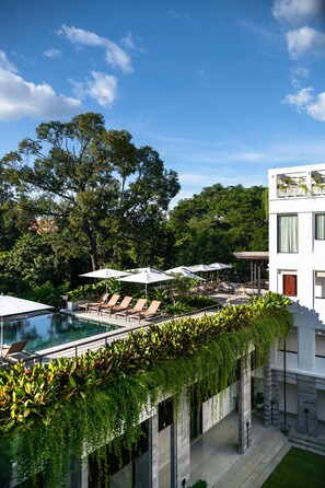 A modern hotel with a rooftop infinity pool, lounge chairs, and a lush green garden. - Treeline Urban Resort (Siem Reap)
