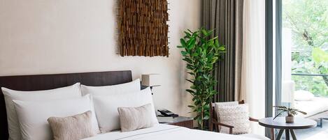 A modern hotel bedroom with a large bed, a bedside table, a chair, a potted plant, and a view of greenery outside.