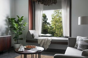 A modern living room with a large window, a sofa, a coffee table, and a potted plant. - Treeline Urban Resort (Siem Reap)