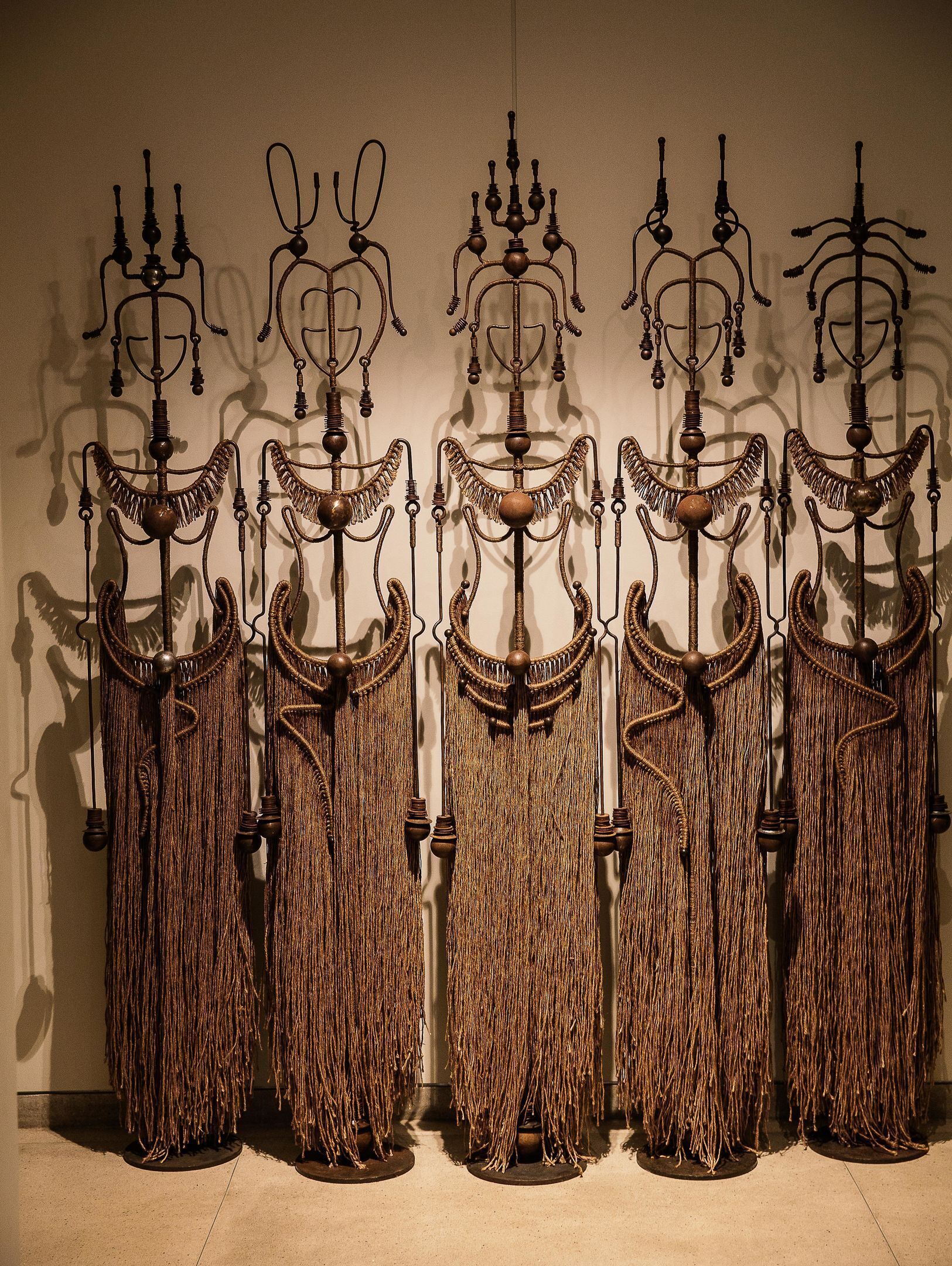 A series of ornate metal chandeliers with tassels hanging from them, displayed against a plain wall.