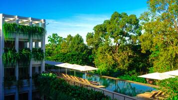 Un área de piscina con sillones de descanso y sombrillas, rodeada de exuberante vegetación y árboles.