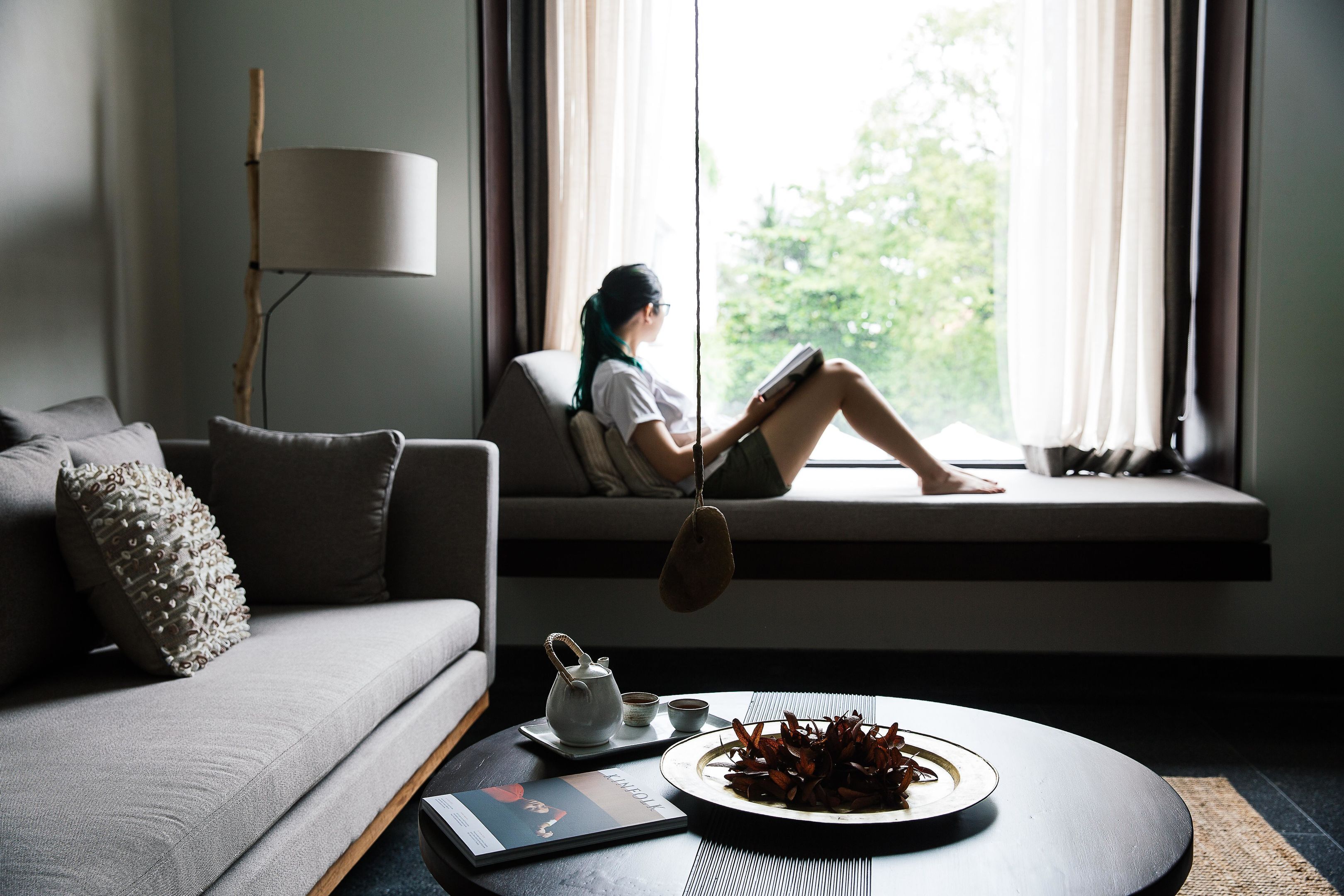 A modern living room with a sofa, a coffee table with a teapot and cups, and a window with a view of greenery.