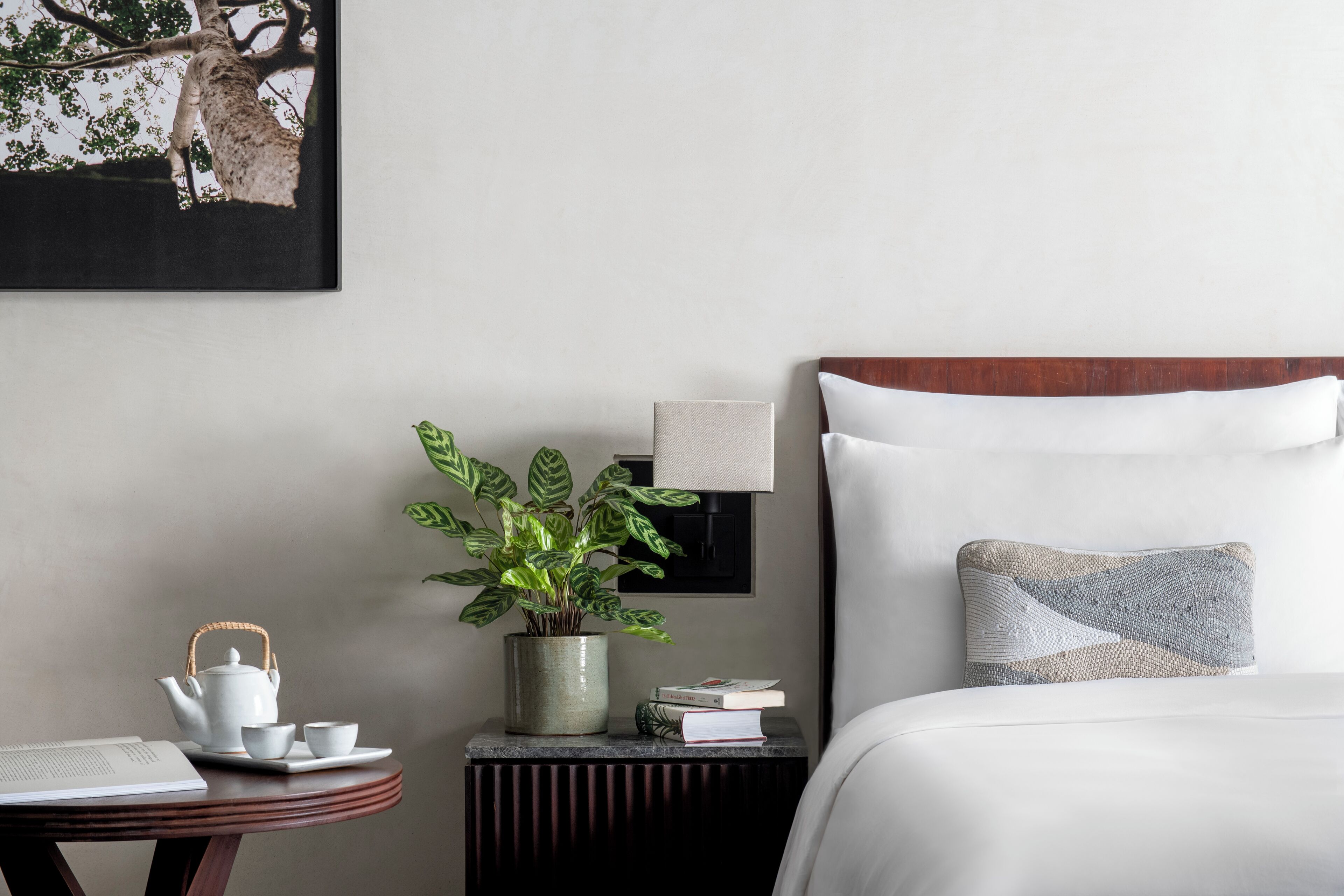 A neatly arranged hotel room with a bed, bedside table, and a small table with a teapot, cups, and a book.