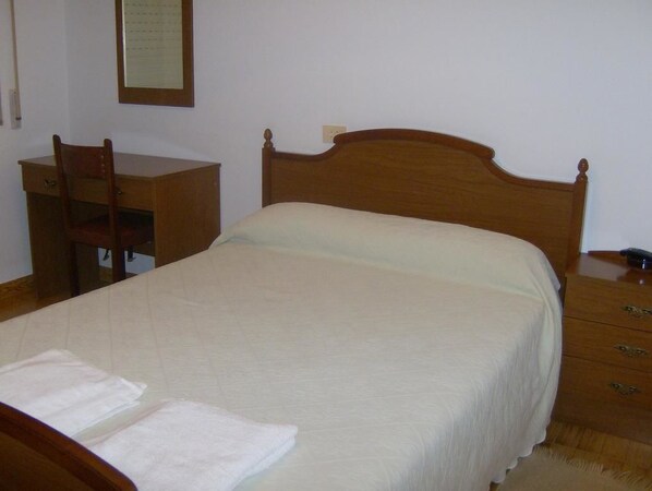 Quarto com cama de madeira, escrivaninha de madeira e uma cadeira.