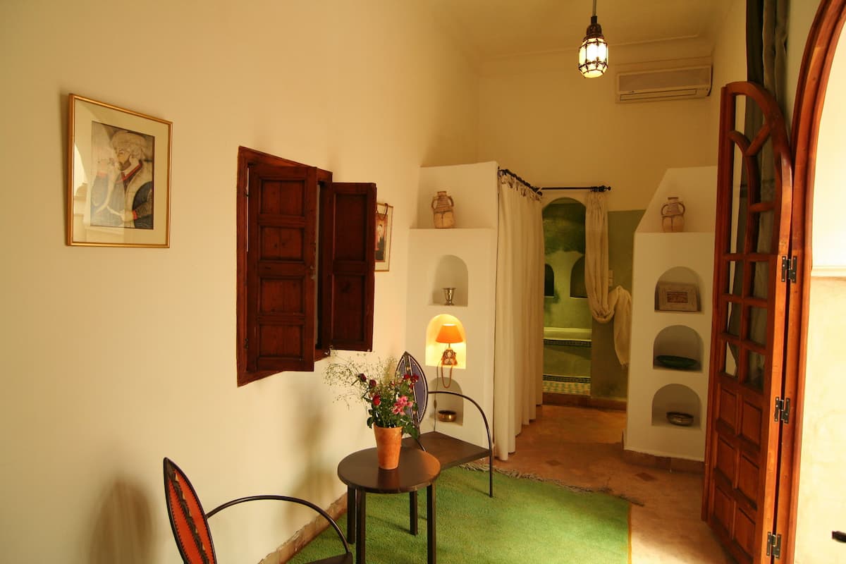 Un pasillo con una puerta de madera, una lámpara, una silla y una planta en maceta.