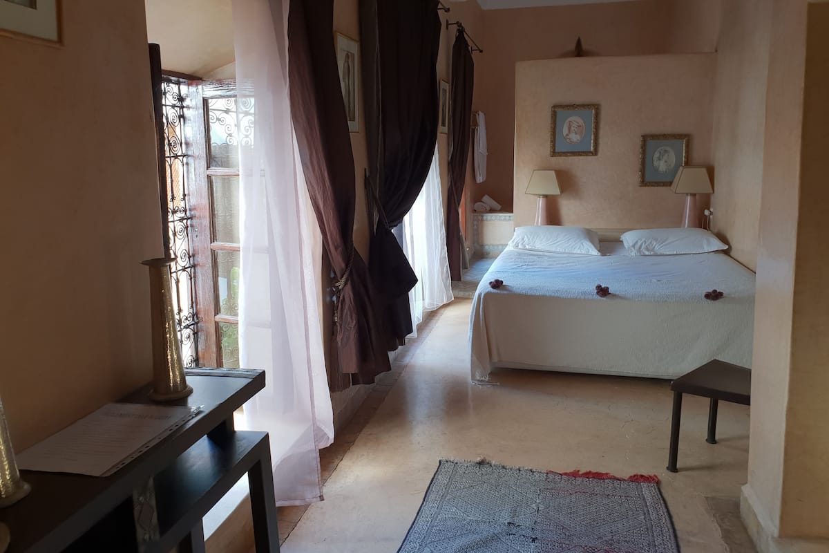 Un dormitorio con cama, mesitas de noche, un escritorio y cortinas.
