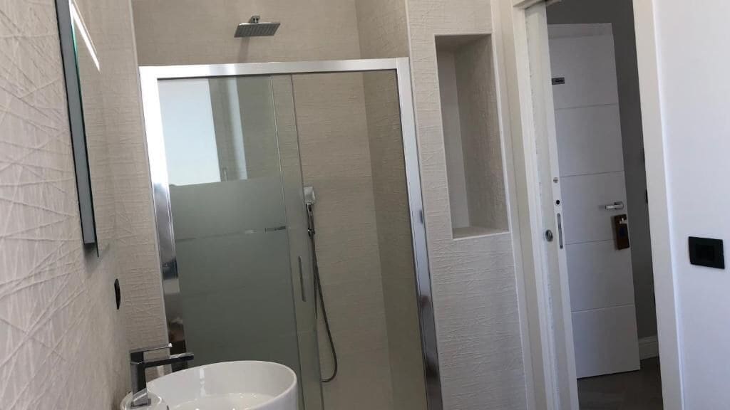 A bathroom with a glass-enclosed shower, a white sink, and a mirror.