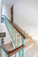 Una escalera con barandales de madera y detalles en color turquesa, que conduce a una puerta con una pequeña planta en maceta a su lado.