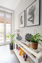 Un área de recepción con una consola blanca, obras de arte enmarcadas, señal de Wi-Fi, un calendario y plantas en macetas.