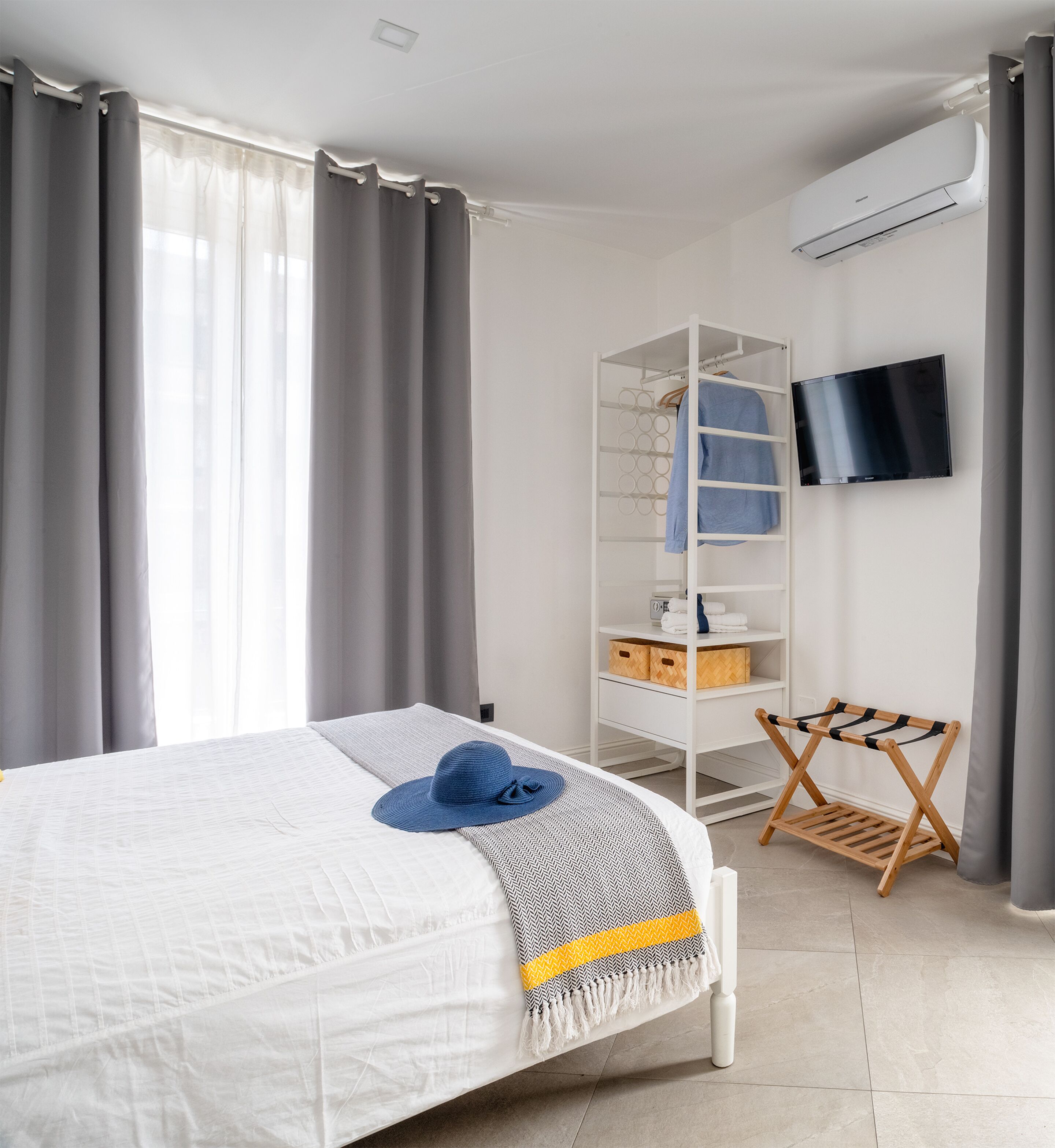 Een slaapkamer met een bed, een kledingkast, een televisie en een droogrek.