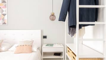 Una camera da letto ordinata e accogliente, con un letto, un comodino bianco, una scaffalatura bianca e una lampada a sospensione.
