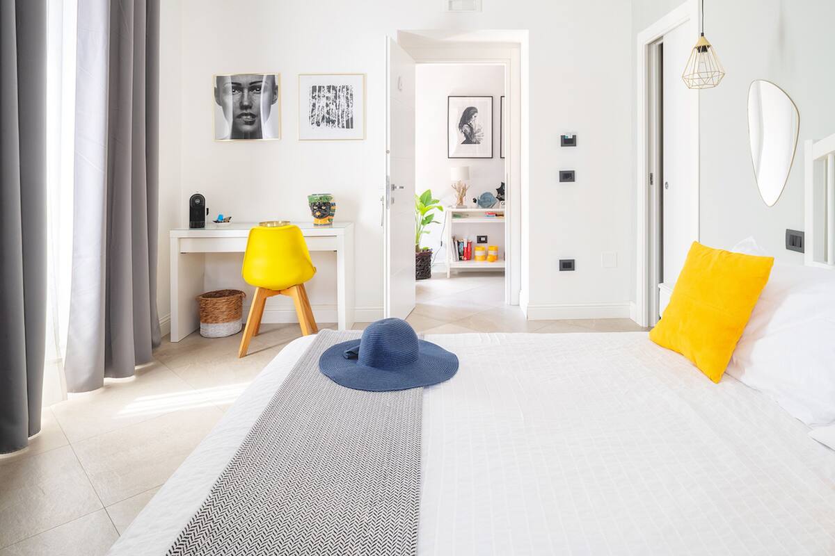 A modern bedroom with a bed, a desk, and a chair. There are framed pictures on the wall.