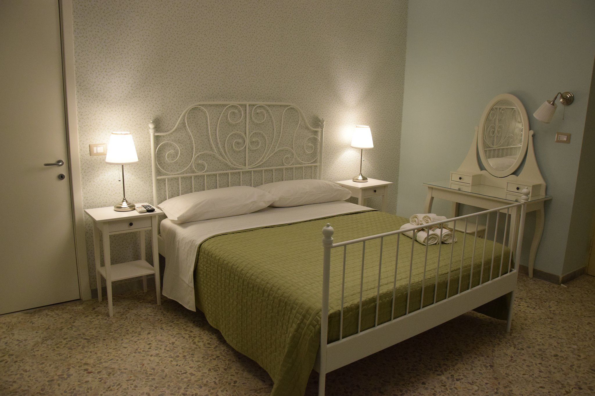 A neatly arranged bedroom with a bed, two bedside tables with lamps, a dresser with a mirror, and a door.