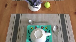A dining table with a placemat, a teapot, a cup, a spoon, a knife, a glass, a pink tulip, a green apple, and a purple flower arrangement. - B&B San Lorenzo (Benevento)