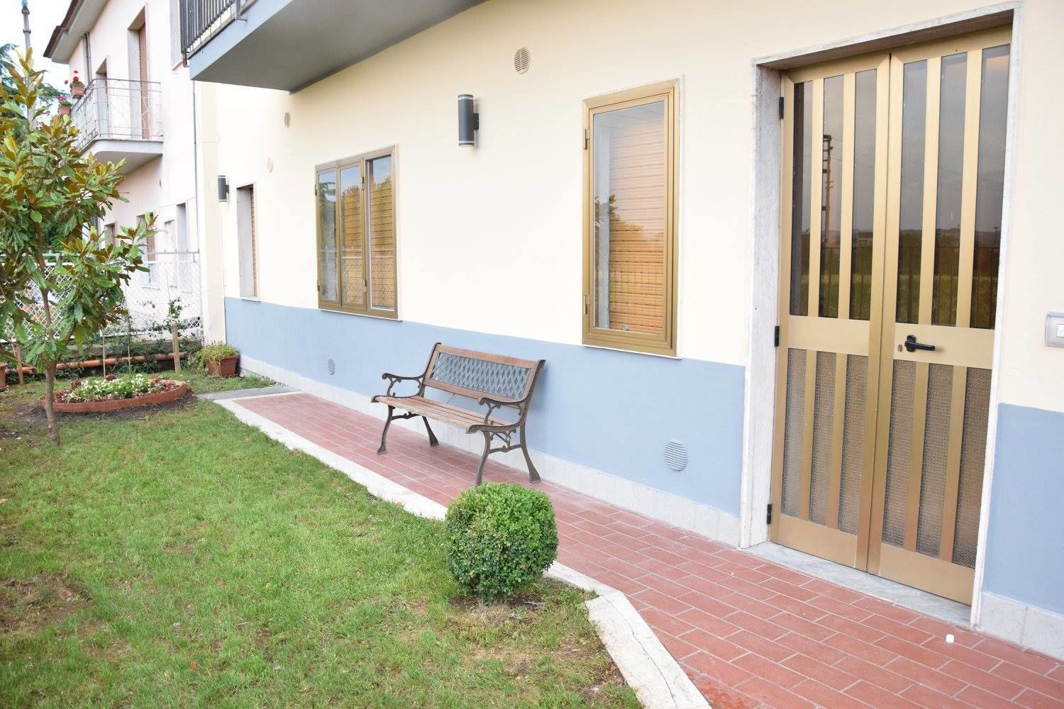 A building with a bench, a small garden, and a door with a metal gate.