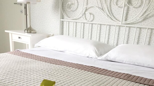 A neatly made bed with a white quilt and a green ribbon, a white nightstand with a lamp, and a decorative metal headboard. - B&B San Lorenzo (Benevento)