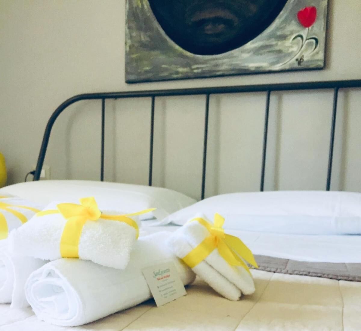 A neatly made bed with white linens and yellow ribbons, a metal headboard, and a wall decoration above.