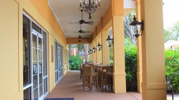 A corridor with ceiling fans, tables, and chairs, leading to a covered area with outdoor views. - Ly86465 - Encantada Resort - 2 Bed 2 Baths Townhome (Kissimmee)
