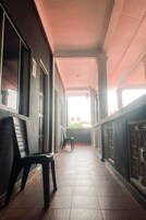 Un pasillo con suelo de baldosas, sillas de plástico negro y vista a un edificio con tejados rojos a lo lejos.