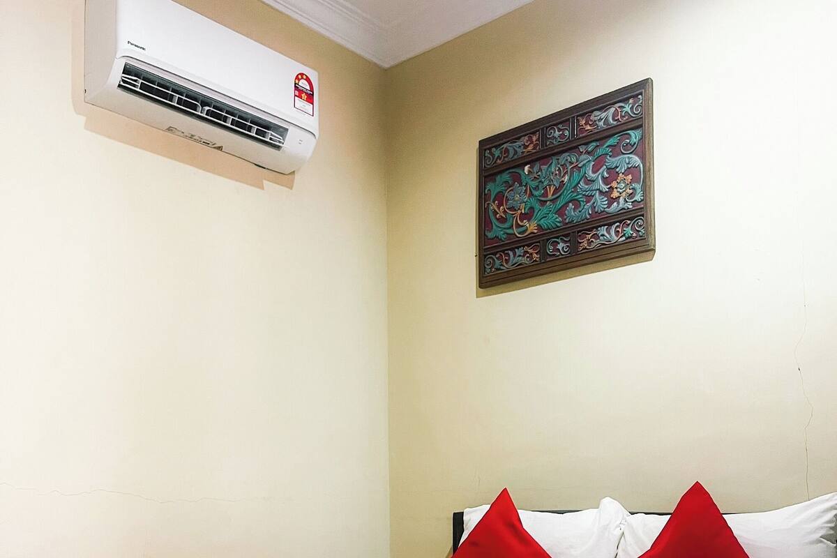 Habitación de hotel con cama, ropa de cama roja y blanca, aire acondicionado de pared y un adorno mural.