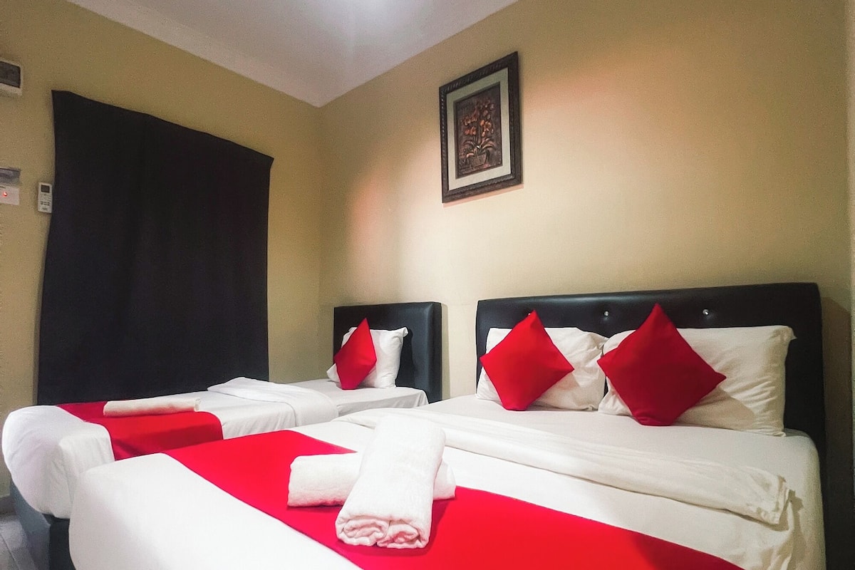 Habitación de hotel con dos camas, cada una con ropa blanca y almohadas rojas, y un cabecero negro.