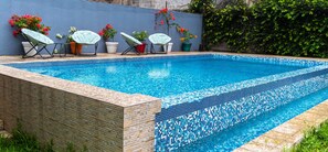 Une piscine rectangulaire aux carreaux de mosaïque bleus, entourée d’un mur de pierre et agrémentée de plantes en pot.