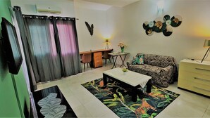 A living room with a sofa, coffee table, and a desk with chairs. - VMD Aparthôtel (Abidjan)