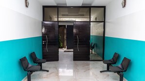 A waiting area with two black chairs, a tiled floor, and a door leading to another room. - VMD Aparthôtel (Abidjan)