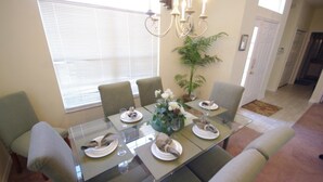 Un comedor con una mesa de vidrio, seis sillas y una araña.