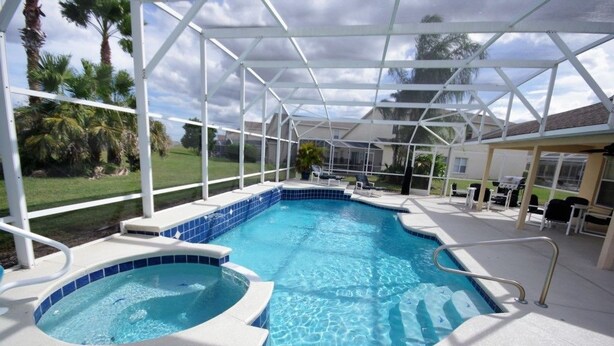 Una piscina techada con jacuzzi, rodeada de palmeras y una zona de terraza.