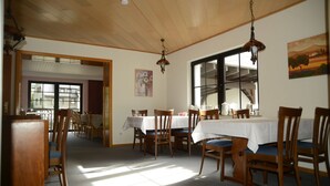 A dining area with wooden tables and chairs, a large window, and a painting on the wall. - Hotel Leise Garni Willingen (Willingen)