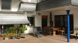 A covered outdoor patio with a dining area, potted plants, and a blue pillar. - Hotel Leise Garni Willingen (Willingen)