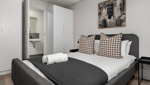 A modern hotel room with a bed, a bathroom, and a cityscape painting. - Greenwich 602 (Cape Town)